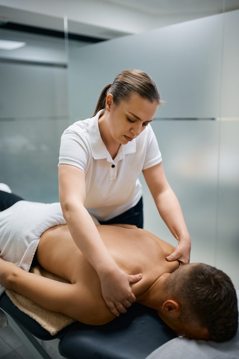 Female massage therapist giving Deep Tissue Massage Camrose to a man's shoulder at physical therapy center at Camrose